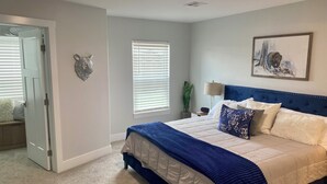 A bedroom with a bed, a door, a window, a wall-mounted lamp, and a painting.