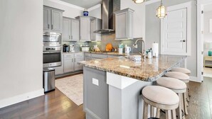 Una cocina moderna con encimeras de granito, electrodomésticos de acero inoxidable y una isla central con taburetes de bar.