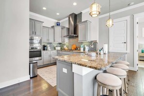 A modern kitchen with granite countertops, stainless steel appliances, and a central island with bar stools. - Sandbar Sunset by Stay on 30a (Inlet Beach)