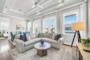 A modern living room with a sectional sofa, a round coffee table, and a dining area with a table and chairs. - Sandbar Sunset by Stay on 30a (Inlet Beach)