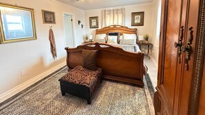 Ein Schlafzimmer mit einem hölzernen Bett, einem Deckenventilator, einem gemusterten Teppich und einer Tür mit einer verzierten Griff.