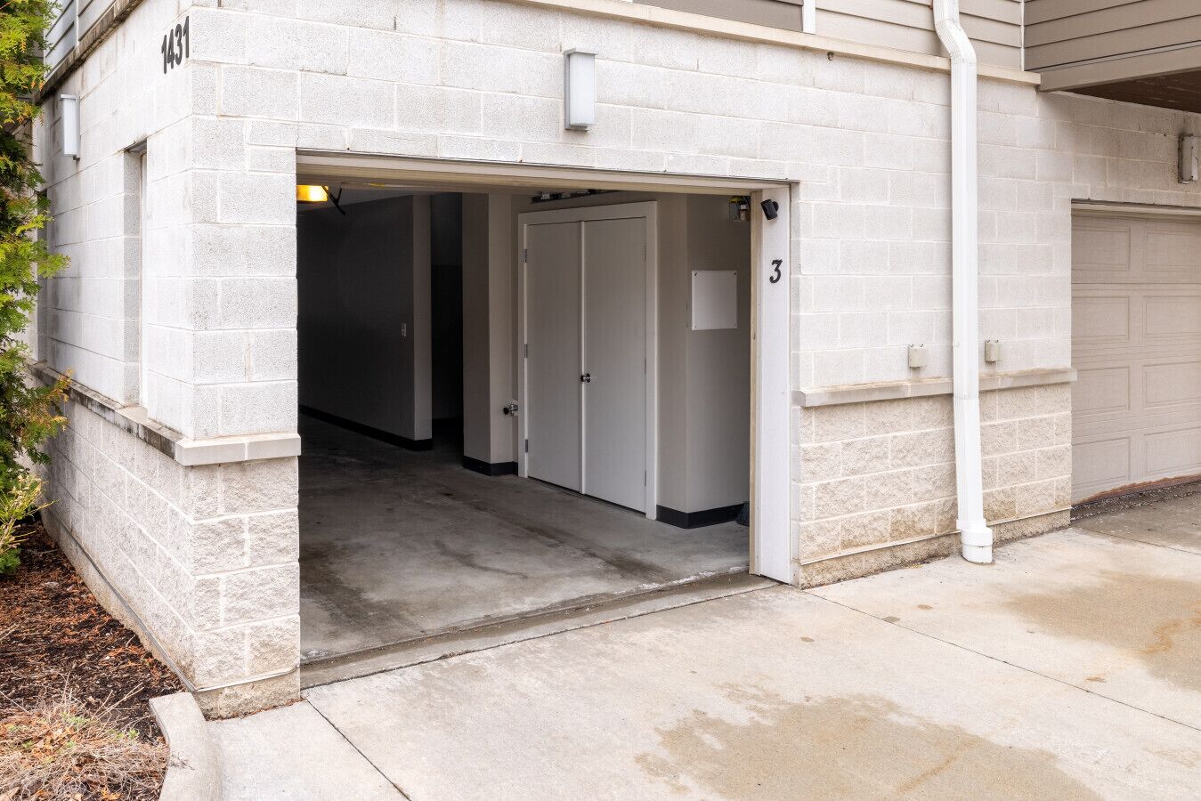 A building entrance with a garage door, a door labeled "3", and a concrete pathway leading to the entrance.