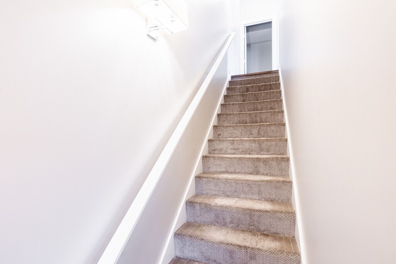 A carpeted staircase with white walls and a door at the top.