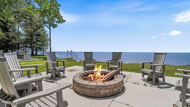 A fire pit surrounded by Adirondack chairs, overlooking a body of water.
