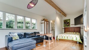 Un salon moderne avec un canapé en cuir, une table à manger, un lit avec une literie à motifs et un téléviseur fixé au mur.