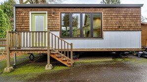 Une maison mobile avec une façade en bois, une porte verte et un petit porche doté d’une balustrade en bois.
