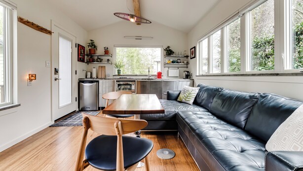 Un espace de vie moderne comprenant un canapé, une table à manger et des chaises. Il y a également un coin cuisine équipé d’appareils électroménagers et une fenêtre qui laisse entrer la lumière naturelle.
