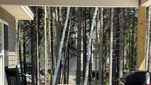 A wooden deck with a picnic table and a grill, surrounded by trees. - Spacious new 2 bedroom home in charming Bass Harbor (Tremont)
