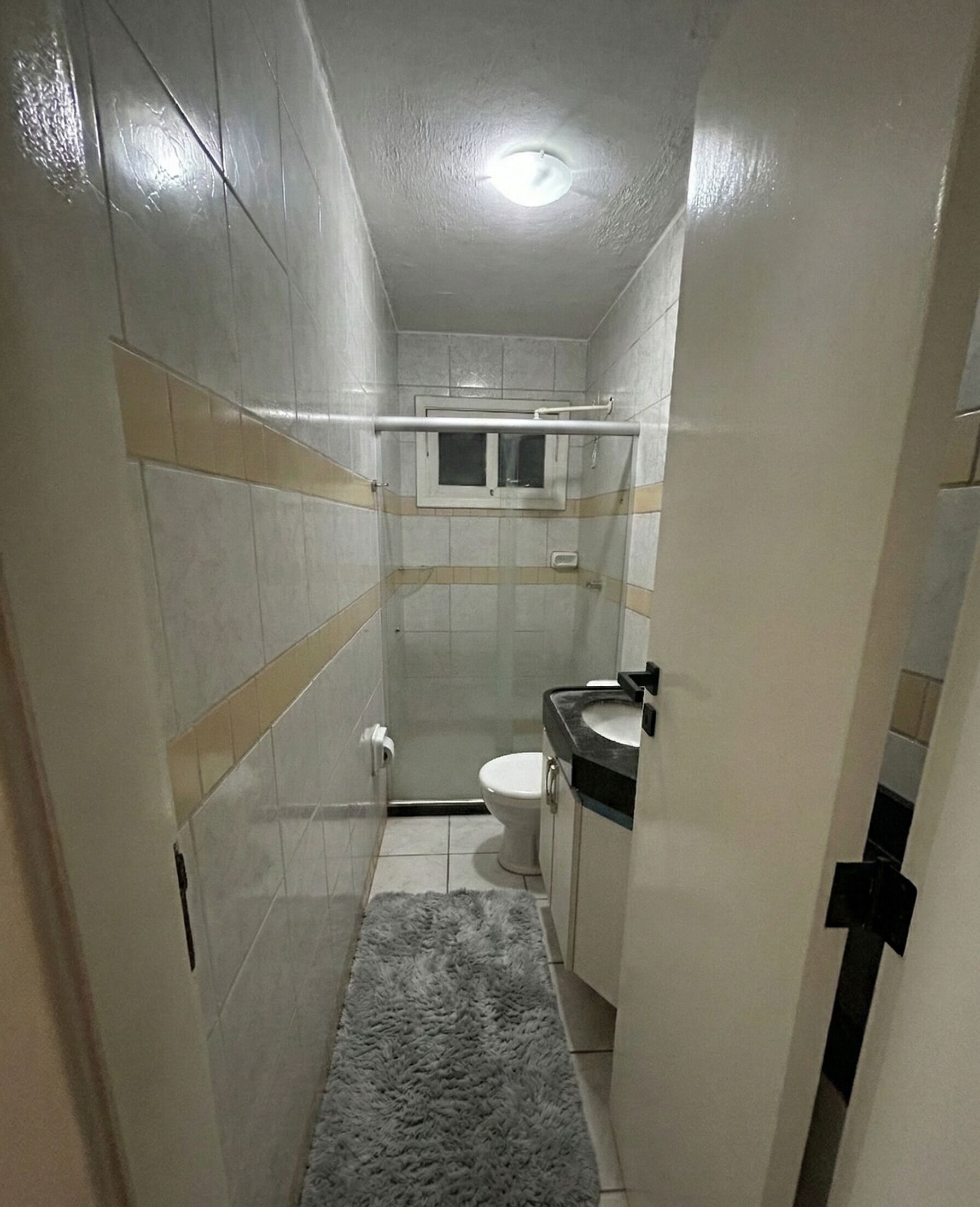 Et aflangt badeværelse med toilet, vask og et vindue.