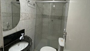 A bathroom with a white toilet, a sink with a black countertop, a shower area, and a mirror.