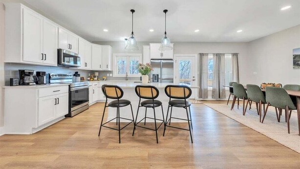 Una cocina moderna con alacenas blancas, electrodomésticos de acero inoxidable y un comedor con mesa y sillas.