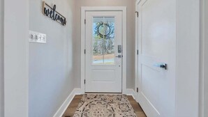 Un pasillo con una puerta blanca, un cartel de bienvenida y una alfombra estampada.