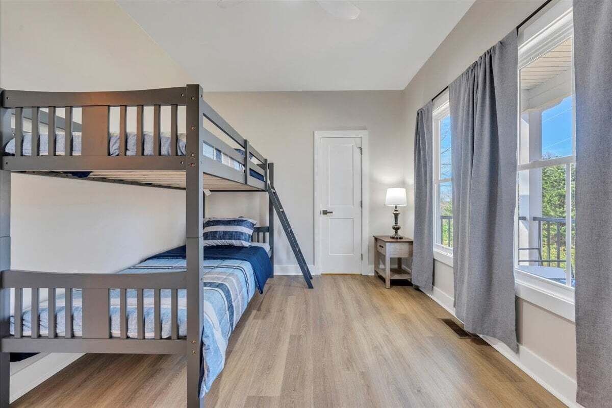A room with a bunk bed, a small table with a lamp, and a window with curtains.