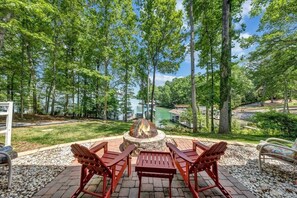 A fire pit surrounded by red Adirondack chairs, overlooking a lake and forested area. - Lake Reflections - Lakefront With Private Dock, & Fire pit (Huddleston)