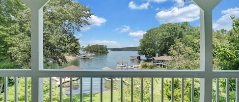 A covered deck with a view of a lake, surrounded by trees and a dock with boats.