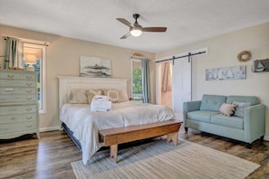 A bedroom with a bed, a bench, a dresser, a sofa, and a ceiling fan. - Kelly Kove - Beach Area Sleeps 14, Private Dock, Pet Friendly (Penhook)