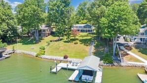 Une propriété au bord du lac, dotée d’un quai, d’un abri pour bateaux et d’une pelouse avec un escalier menant à une maison.