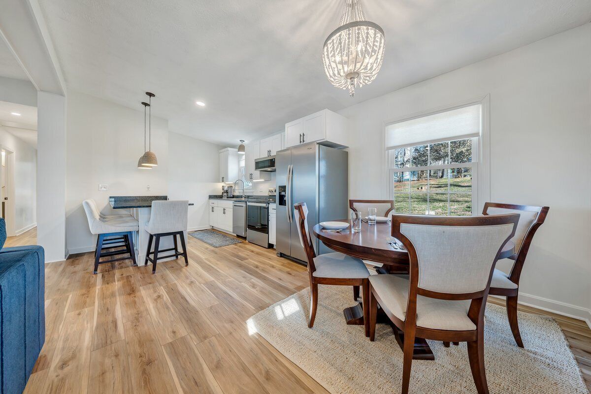 A modern kitchen with a dining area, featuring a large island, stainless steel appliances, and a chandelier.