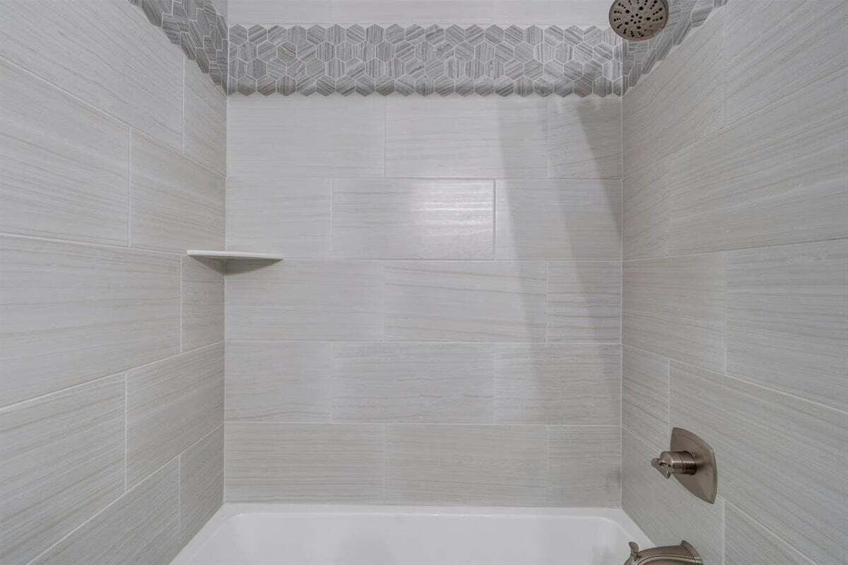 Une salle de bain avec des murs recouverts de carreaux blancs, un espace douche et des toilettes dotées d’un robinet moderne.