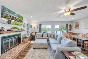 A spacious living room with a fireplace, a large sofa, a dining table, and a ceiling fan. - Lakeside Sunsets - Private Dock, Hot Tub & Firepit (Moneta)