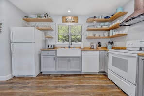 A modern kitchen with white cabinetry, wooden shelves, a built-in oven, and a window with a view of greenery. - Lakeside Sunsets - Private Dock, Hot Tub & Firepit (Moneta)