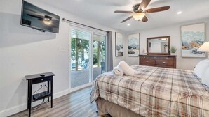 A bedroom with a bed, a TV, a ceiling fan, a dresser, and a sliding glass door to a balcony. - Lakeside Sunsets - Private Dock, Hot Tub & Firepit (Moneta)