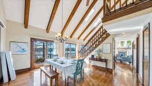 A spacious dining area with a wooden table and chairs, a staircase, and large windows. - Pine Knob Point - Lakehouse w/ Private Dock (Moneta)