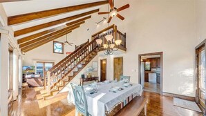 A spacious dining area with a high ceiling, wooden beams, and a staircase leading to an upper level. - Pine Knob Point - Lakehouse w/ Private Dock (Moneta)