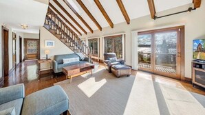 A spacious living area with a staircase, wooden beams, large windows, and a view of the outdoors. - Pine Knob Point - Lakehouse w/ Private Dock (Moneta)