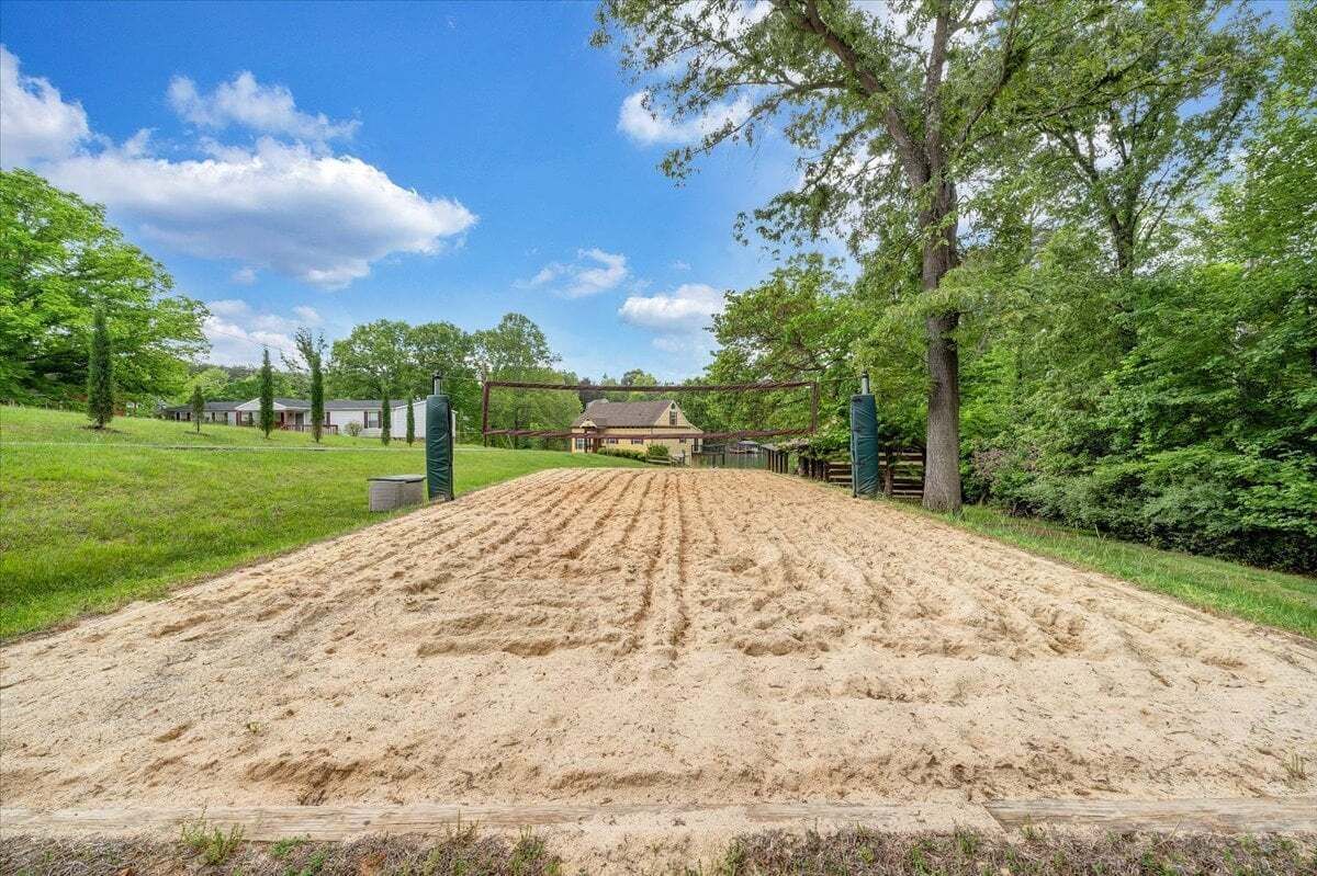 A sandy equestrian arena with a wooden fence, surrounded by green grass and trees.