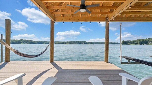 Eine Holzterrasse mit einer Hängematte, weißen Liegestühlen und einem Deckenventilator.