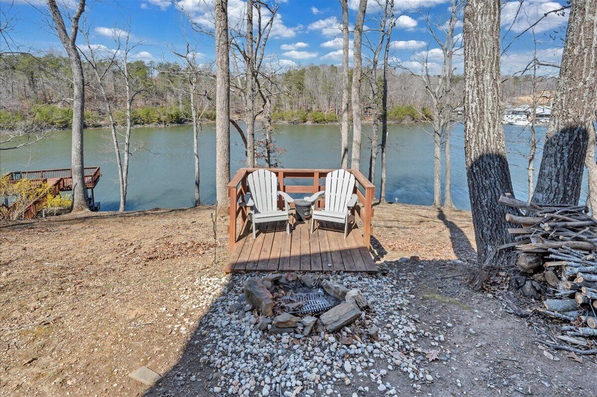 A wooden deck with Adirondack chairs overlooking a lake, surrounded by trees.