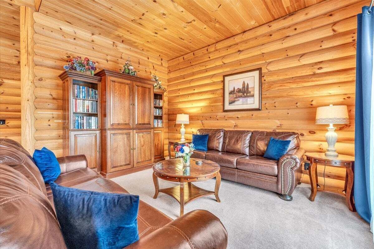 A cozy log cabin interior with a leather sofa, a wooden coffee table, and a bookshelf.