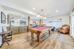 Ein Billardtisch in einem Raum mit Holzboden, einem Ledersessel und einer Bar im Hintergrund.