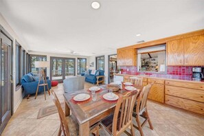 A spacious living area with a wooden dining table set for four, a blue sofa, and a kitchen with wooden cabinets and a red backsplash. - Lake Harmony - Lakefront Home w/ Private Dock, & Fire Pit (Huddleston)