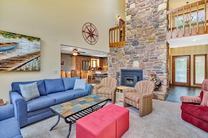 A spacious living area with a stone fireplace, a blue sofa, patterned armchairs, and a red ottoman. - Dancing Water - Sleeps 10, Private Dock, Game Room & Hot Tub (Moneta)