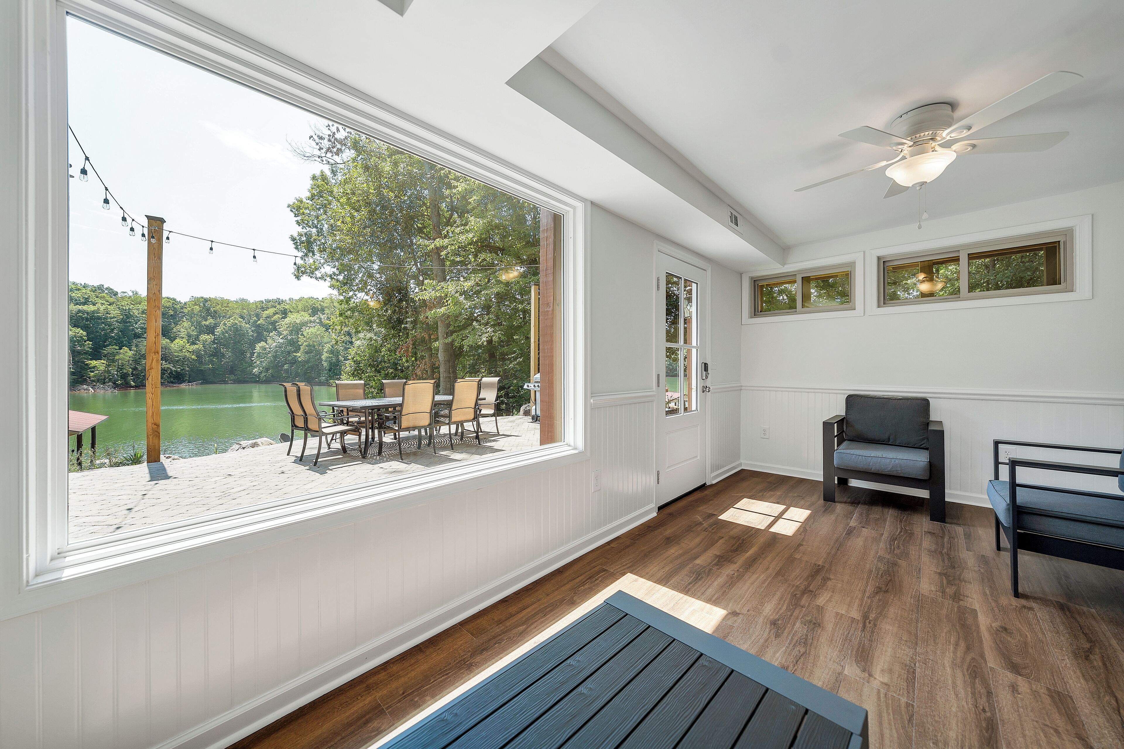 Ein Zimmer mit großen Fenstern mit Blick auf einen See, einem Deckenventilator und einer Sitzecke mit Tisch und Stühlen.