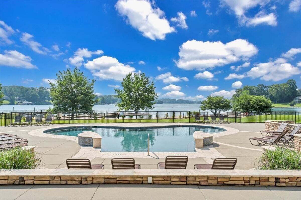 A pool area with a view of a lake, surrounded by trees and a stone wall.
