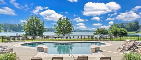 A pool area with a view of a lake, surrounded by trees and a stone wall.