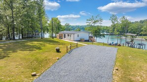 Una propiedad junto al lago con un camino de grava que conduce a un edificio blanco, rodeado de árboles y vistas al lago.