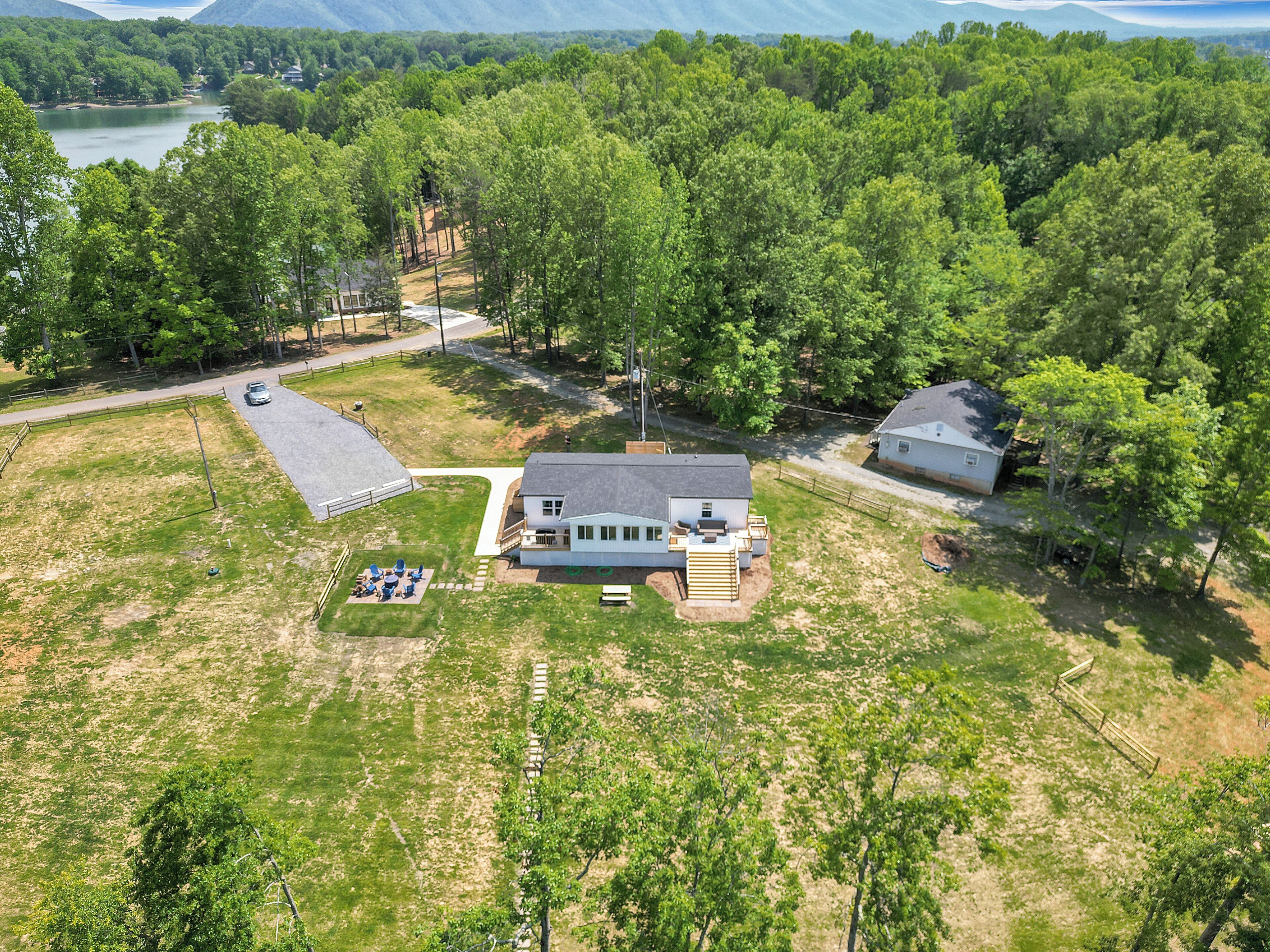 An aerial view of a house surrounded by a large yard with a lawn, a patio, and a small deck.