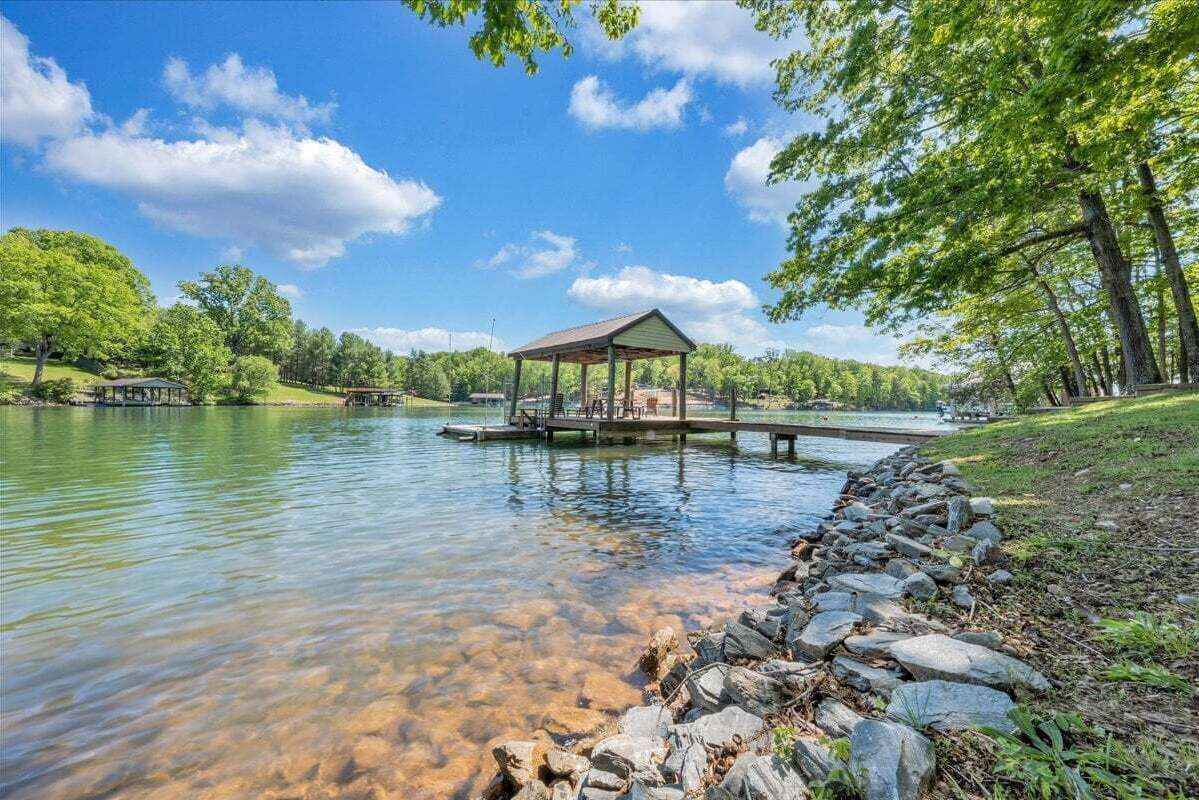 A tranquil lakeside setting with a gazebo on a dock, surrounded by lush greenery and clear water.