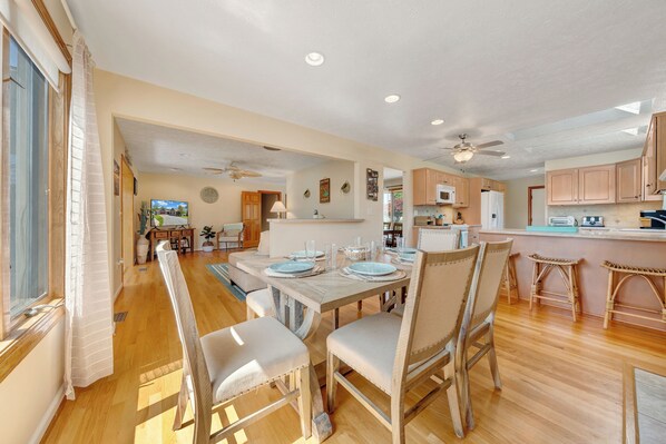 A spacious dining area with a long table set for four, wooden flooring, and a ceiling fan. - Stargaze - Lakefront With Private Dock (Huddleston)