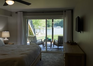Ein Schlafzimmer mit Bett, Nachttisch, Lampe, Fernseher und Blick auf eine Terrasse und einen See.