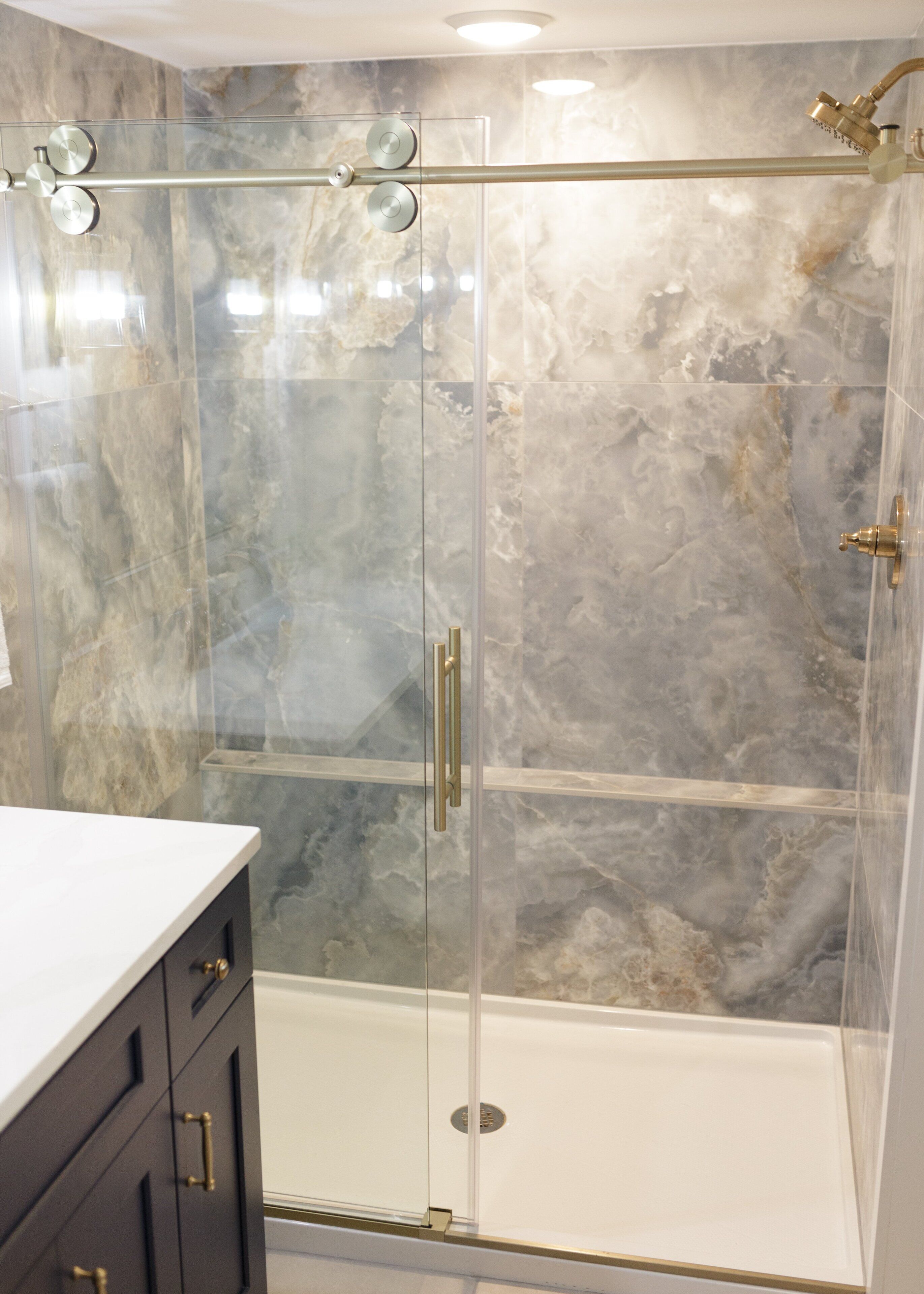 Un baño moderno con ducha de vidrio, paredes de mármol y encimera blanca.