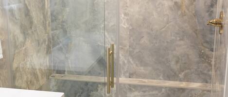 Un baño moderno con ducha de vidrio, paredes de mármol y encimera blanca.