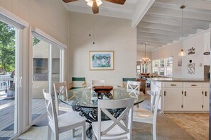 Un coin repas avec une table en verre et des chaises blanches, une cuisine avec des meubles blancs et un ventilateur de plafond.