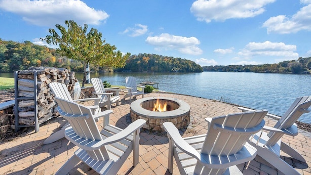 A lakeside patio with Adirondack chairs, a stone fire pit, and a stone wall. - Paradise Point - Lakefront Home With Private Dock! (Goodview)