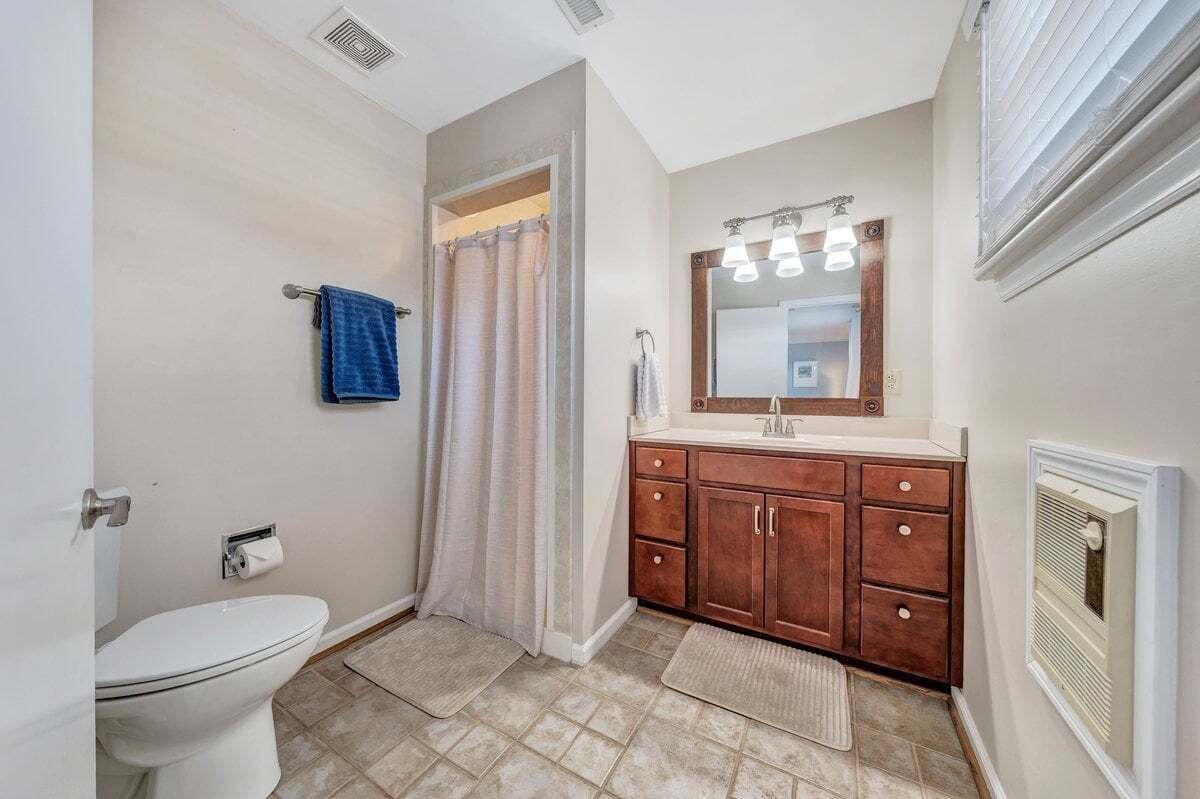 A bathroom with a toilet, a sink with a mirror, wooden cabinets, and a shower curtain.