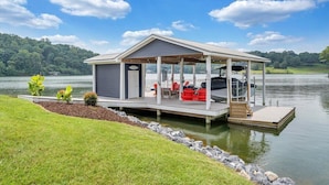 A lakeside cabin with a covered deck, outdoor seating, and a dock. - Paradise Point - Lakefront Home With Private Dock! (Goodview)